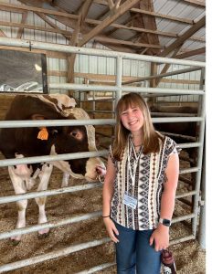 UConn IDEA Grant recipient Claire Zess, smiling, standing in a barn in front of a metal barrier with a black and white cow.