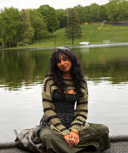 Image of student Harri Srivastava sitting on a ledge with a lake in the background and woods behind the lake.
